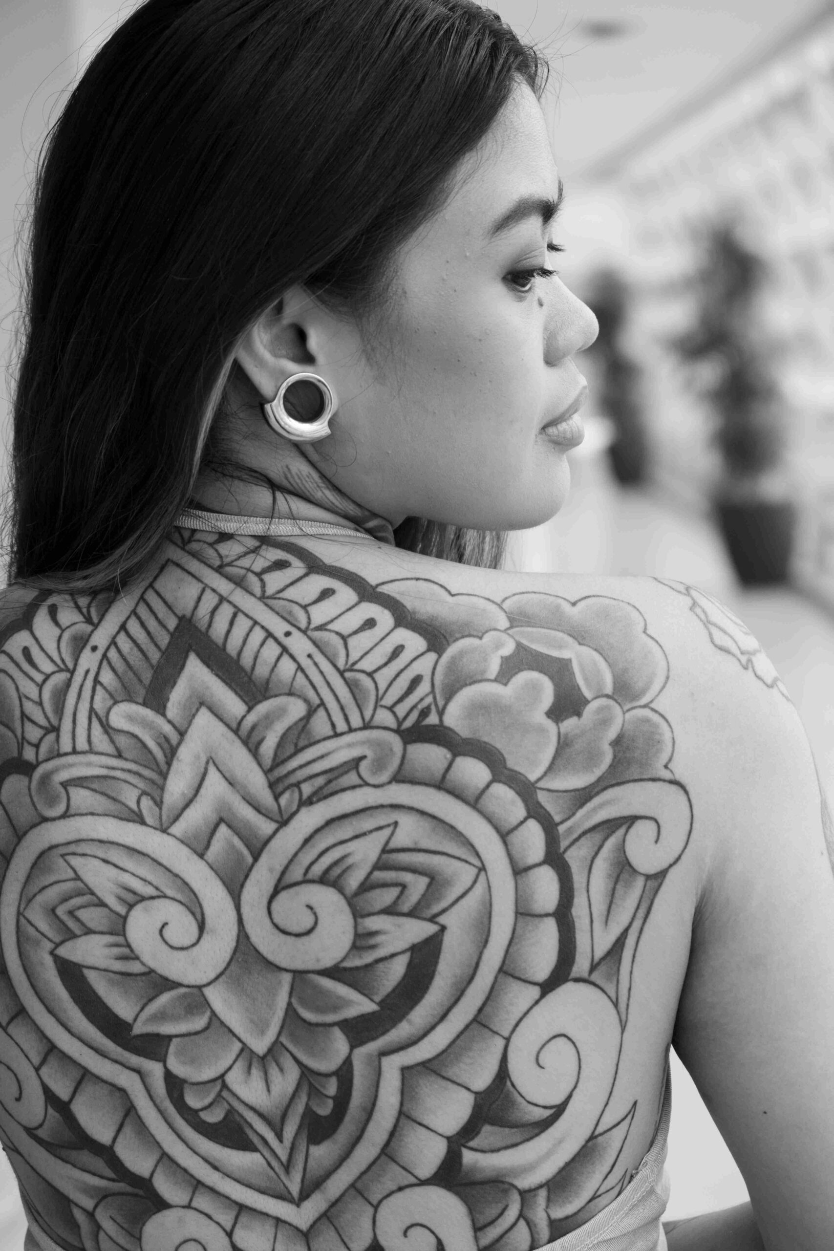 Black and white portrait of a woman with a large floral tattoo across her back.